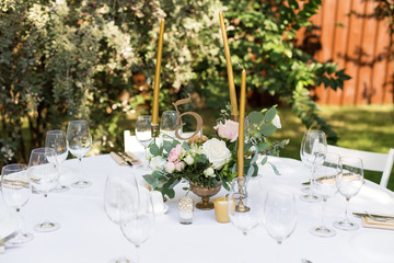 Wedding table setting decorated with fresh flowers in a brass vase. Wedding floristry. Banquet table for guests outdoors with a view of green nature. Bouquet with roses, eustoma and eucalyptus leaves