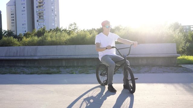 SLOW MOTION Portrait of young bmx rider with cap putting hands on handers and getting ready on bmx bicycle in park on sunny summer day