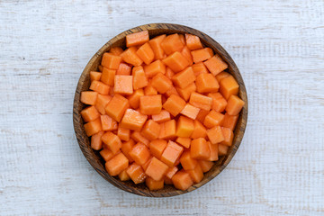 Slices of sweet papaya in coconut bowl on white wooden background, close up