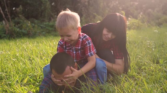 happy family teamwork outdoors have fun concept outdoors slow motion video. mom dad and son take a photo with a smartphone in nature are sitting on the grass have fun playing. mom lifestyle girl dad