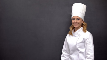 Positive female chef posing on blackboard background, healthy nutrition concept