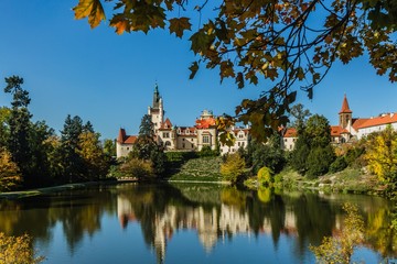 Obraz premium Pruhonice, Czech Republic - October 7 2019: Scenic view of famous romantic castle over a lake with its reflection in water. It is standing on hill in a public park. Sunny autumn day with blue sky. 