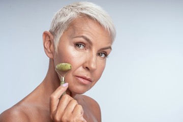 Close up of a pretty and healthy lady using jade roller on a side of her face