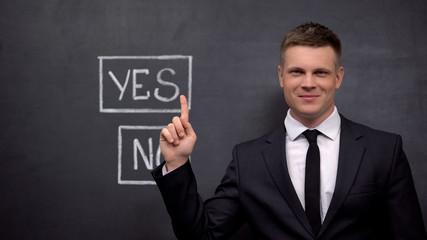 Smiling businessman showing yes button painted on blackboard, investment