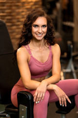 Beautiful fitness brunette woman is sitting in training apparatus for legs