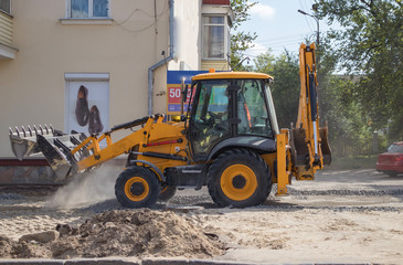 Orange excavator on wheels works in the city