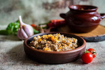 Buckwheat porridge with meat and onions on a clay plate, a clay pot with buckwheat on a wooden stand