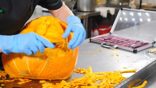 All Saints Day celebration. Part of american holiday activities. Closeup shot of hands in gloves carving from a pumpkin Jack-o. Cutting Scary glowing halloween pumpkin . Special knives. Shot in 4k