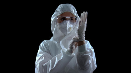 Person in protective suit wearing rubber gloves against dark background, toxins