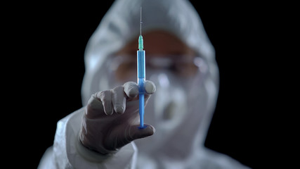 Pharmacologist showing syringe at camera against black background, illegal lab