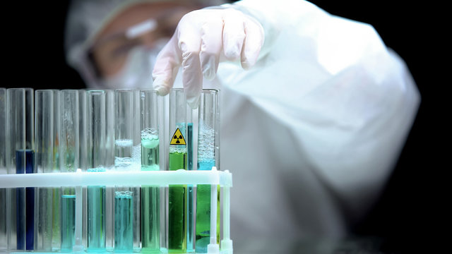 Lab worker taking test tube with green radioactive sample, ecological pollution