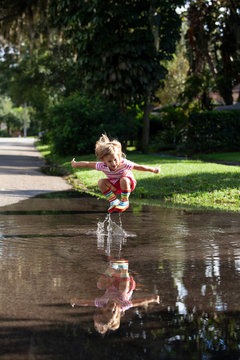 A little girl wearing rainbow rain-boots jumping and splashing in her reflection in a puddle
