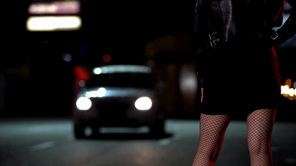 Female in leather jacket and fishnet stockings standing on street, prostitution