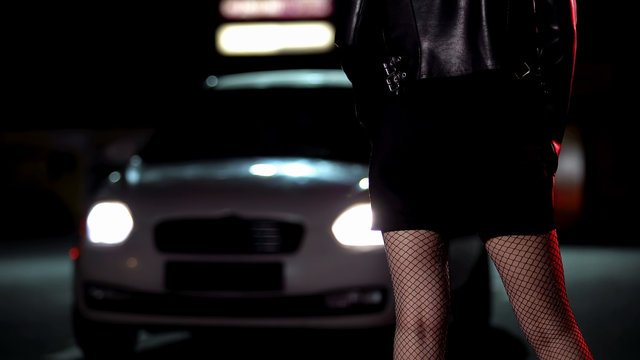 Car driving to prostitute in provocative clothing on dark street, night life