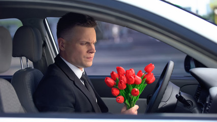 Unhappy man looking at bunch of tulips and deciding to drive away, breakup