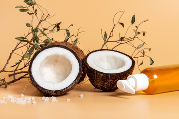 Sliced coconut, coconut oil, dry branches and salt on a soft orange background. Skincare concept, healthy lifestyle.
