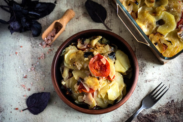 Vegetarian dish: vegetables baked with Basil in the oven. Potatoes with onions and tomatoes in a clay plate on a vintage gray background