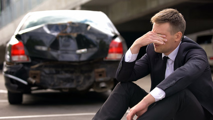 Fototapeta na wymiar Desperate man sitting asphalt on crashed car background, automobile accident