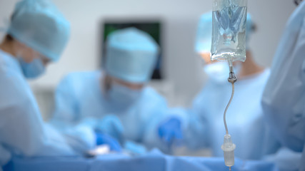 Medical drip bag on background of surgeon team working in operation room