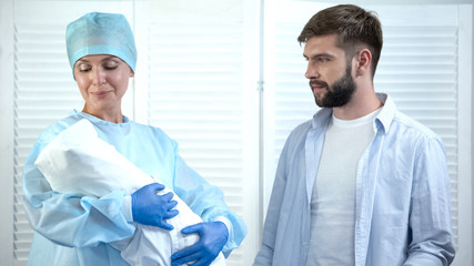 Obraz premium Nurse looking at child before giving baby to father, leaving maternity hospital
