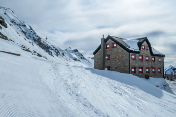 A big alpine cottage covered snow in Mölltaler Gletscher, Austria. Thick snow covers the surroundings. Clear weather. Perfectly groomed slopes. Beautiful and serene mountains covered with snow.