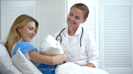 Happy mother holding newborn baby, smiling doctor looking at child, motherhood