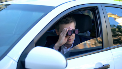 Man in suit spying from car using binoculars, private detective investigation