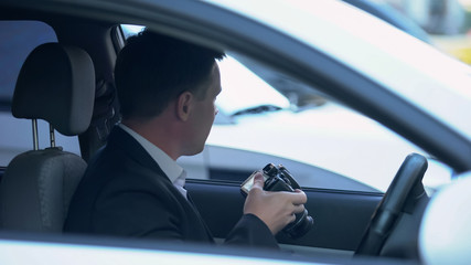 Private agent with camera sitting in car, searching for evidence of cheating