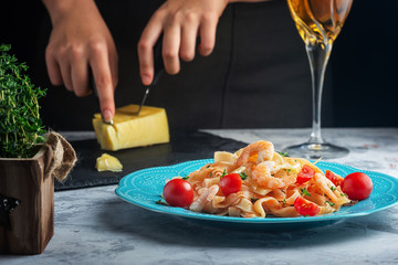 Girl slices parmesan cheese to decorate dinner. Spaghetti with tomato sauce and shrimp. Selective focus.