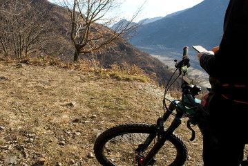 man with an electric bicycle, e-bike, ebike, check the map path on the mobile phone, mountains, autumn, sunset, Piedmont, Ossola Valley, Italy