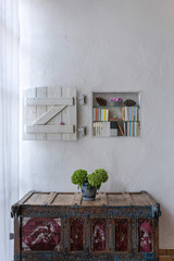 beautiful cabinet with flowers in front of white wall with books and shutter