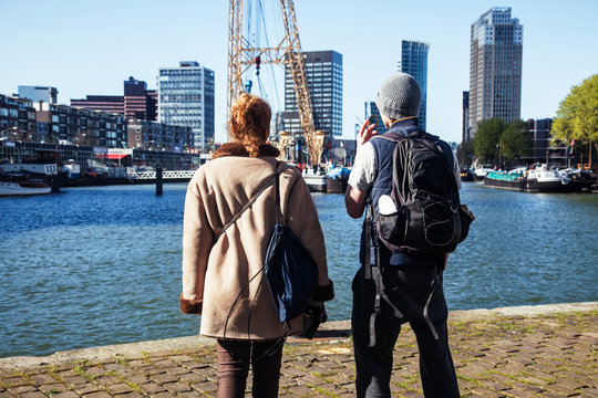 Young Couple Tourists Looking And Pointing To Rotterdam City Harbour, Future Architecture Concept, Industrial Lifestyle People