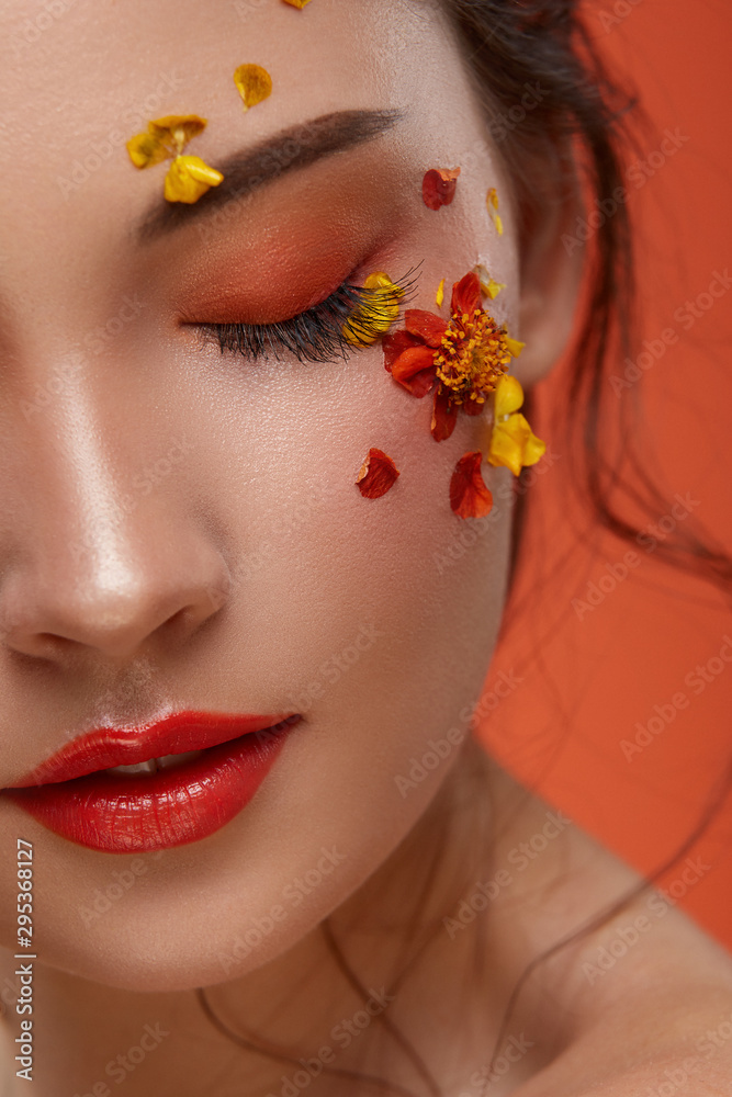 Wall mural close-up of half woman face with beautiful flowers and orange make up