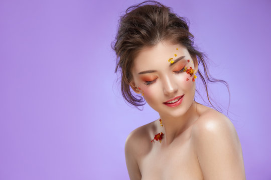 pretty female with elegant colorful make-up and natural fowers looking down isolated on purple