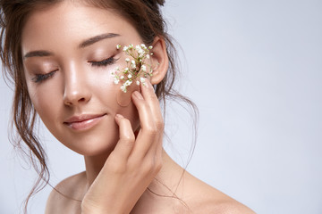 pretty female with nude make-up touching a cheek with plaster and flowers on it