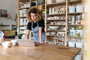 Woman pottery artist using laptop in art studio 