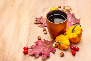 Autumn cozy mood composition. Hot tea in ceramic glass, fall leaves, pumpkins, briar, hazelnuts