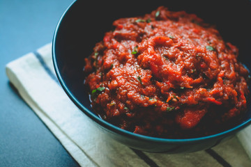 Red vegetable sauce. Sauce of baked bell pepper and eggplant with parsley. Dark blue bowl and napkin.