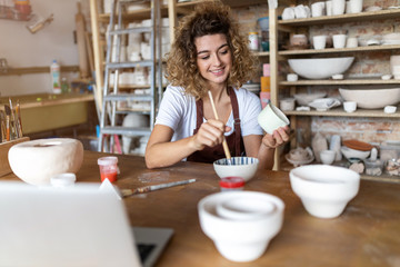 Craftswoman painting a bowl made of clay in art studio