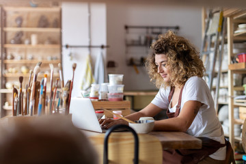 Woman pottery artist using laptop in art studio 