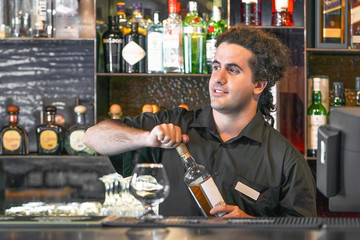 Portrait of caucasian bartender man opens a bottle of whiskey for a hotel bar customer. The concept of service. Focus on the bartender.  