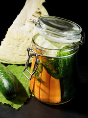 Jar with fermented vegetables. Fermented, canned vegetarian food concept. Cabbage, cucumber, dill, markov. Sauerkraut in a glass jar on a black kitchen table. The concept of canned food. Close-up.
