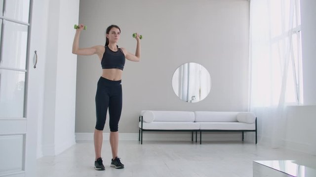 Raise the dumbbells over your head performing exercises for the shoulders. Training at home in the apartment