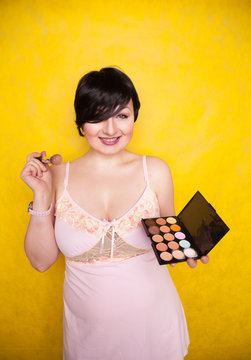 Happy plus size woman having fun with make-up palette set and brush. Professional multicolor eyeshadow face corrector palette.