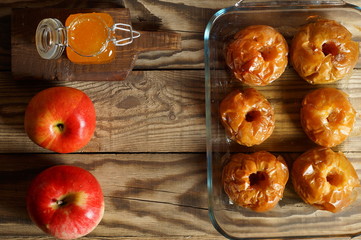 Red, fresh apples and baked apples with honey in the oven in a transparent, glass form on a wooden...