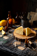homemade two tasty slices of baked lemon biscuit cake with powdered sugar on top stands on wooden board on rustic table with lemons, old bottles opposite concrete wall, selective focus