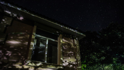 Old house with a Ghost in the forest at night or Abandoned Haunted Horror House in fog. Old mystic building in dead tree forest. Trees at night with moon. Surreal lights. Horror Halloween concept