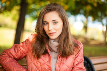 Young stylish woman in a salmon down jacket posing on a background of autumn park