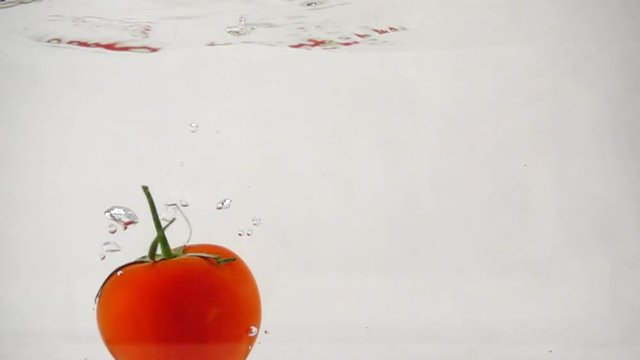 One ripe red tomato rotating dive underwater, slow motion close-up, slow motion close-up, on a white background. Full HD Video.