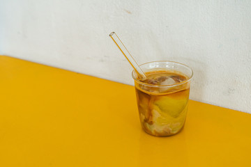Iced coffee mixed with soy milk Laying solitary on a yellow table in front of a white wall